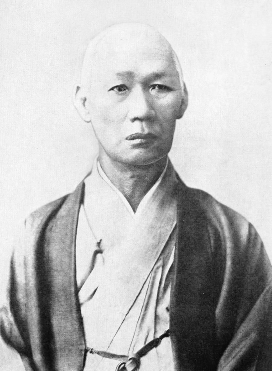 Black-and-white head-and-shoulders photograph of Nakahama Manjirō as an older man with a shaved head, wearing a dark kimono jacket over a light kimono, looking at the camera