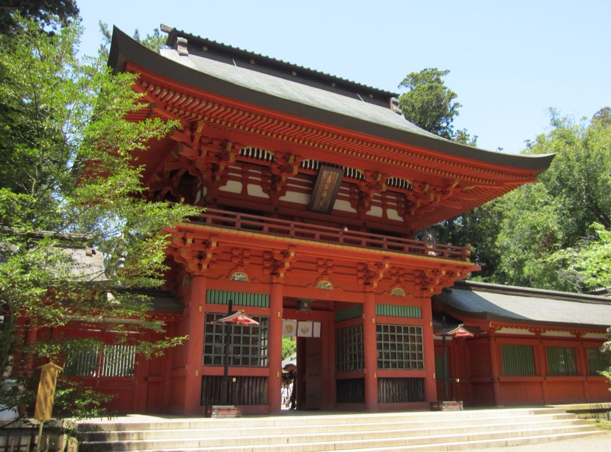 The two-storey vermilion tower gate of Katori Jingu with a dark roof, stone steps in front and green trees around it, photographed in May 2012