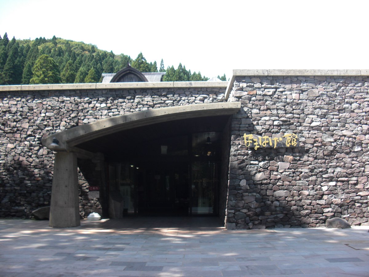 The stone-walled entrance of the Namahage Museum in Oga, Akita, with a curved concrete canopy and wooded hills behind